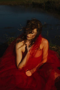 Young woman wearing red dress while sitting on land