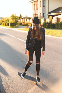 Young woman with skateboard standing on road during sunny day