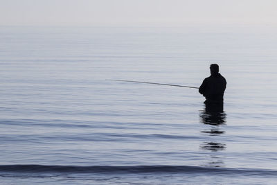 Rear view of silhouette man in sea against sky