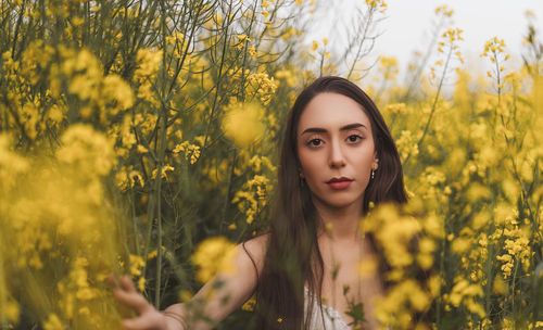 Portrait of young woman standing amidst yellow flowering plants on field