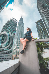 Woman sitting against modern buildings in city