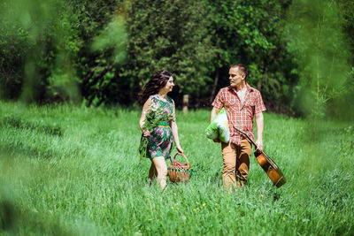 Couple with guitar and basket walking on grassy land