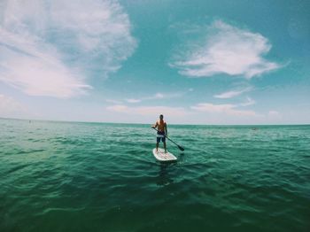 Man paddleboarding amidst sea against sky