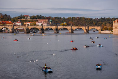 Charles bridge over vltava river against sky with people on paddling boats 