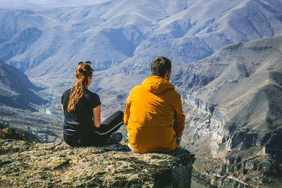 Rear view of couple sitting on cliff against mountains