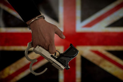 Cropped hand of male criminal holding gun against british flag