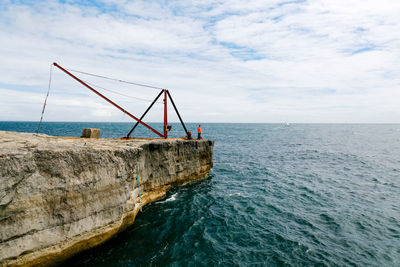 Man standing on cliff by sea against cloudy sky