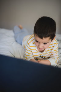 Focused little boy in casual wear browsing laptop while spending free time in bedroom at home
