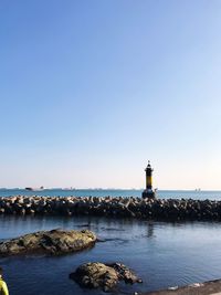 Lighthouse by sea against clear blue sky