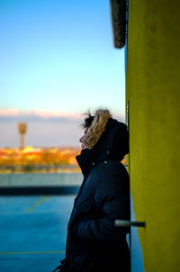 Side view of man standing by yellow wall against blue sky