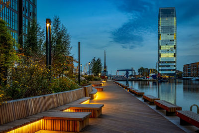 Footpath by illuminated buildings against sky at dusk