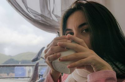 Close-up portrait of young woman drinking coffee at home 