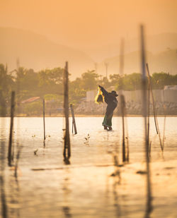 Man standing by lake against sky during sunset