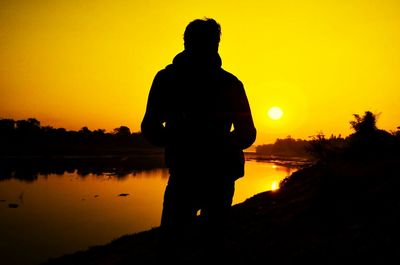 Silhouette man standing by river at sunset