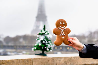Cropped hand of woman holding gingerbread cookie against building
