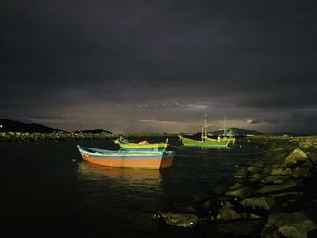 Sailboats moored on sea against sky at night