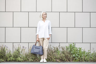Smiling young woman standing against white wall