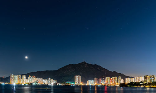 Illuminated city by sea against sky at night