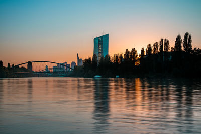 Scenic view of river by buildings against sky during sunset