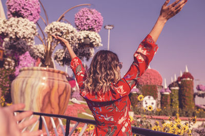 Rear view of young woman standing in ornamental garden against sky 