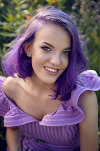 Portrait of a teenage girl with purple hair and an earring in her nose lying in the grass in nature