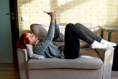 Girl using phone while lying on sofa at home