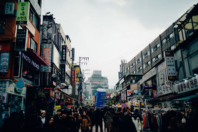 People walking on street amidst buildings in city against sky