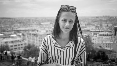 Portrait of smiling young woman standing against cityscape