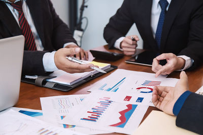 Midsection of businessman and colleague working over graphs on table