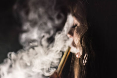 Close-up of woman smoking cigarette against black background