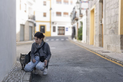 Woman with cat crouching on street in city