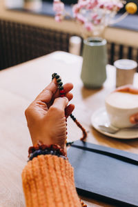 Close-up of hand holding mala beads on a wooden  table