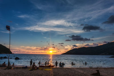 People on beach against sky during sunset