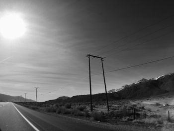 Road by electricity pylon against sky