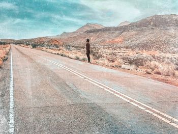 Man standing on road by mountain against sky