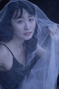 Portrait of young woman seen through netting against black background