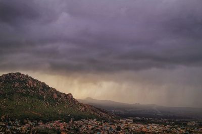 Aerial view of city by mountain against storm clouds