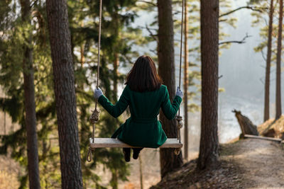 Rear view of woman sitting by tree trunk in forest