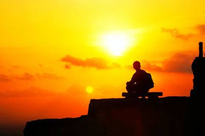 Silhouette man sitting on rock against orange sky