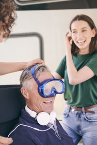 Siblings having fun with grandfather wearing swimming goggles and headphones at campsite