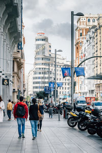 People walking on road against cloudy sky