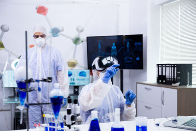 Scientist wearing virtual reality simulator colleague in background at laboratory