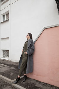 Full length of young woman standing against wall of building