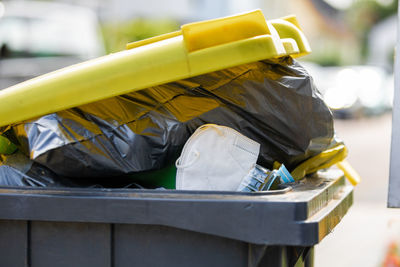 Full garbage trash can with ffp2 face mask standing at sidewalk waiting to get empty