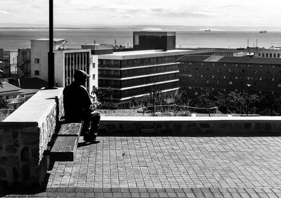 Full length of man on railing by sea against sky in city