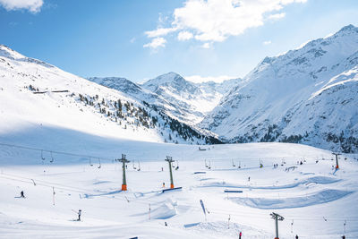 Chairlifts passing through snowy hill with skiers against cloudy sky