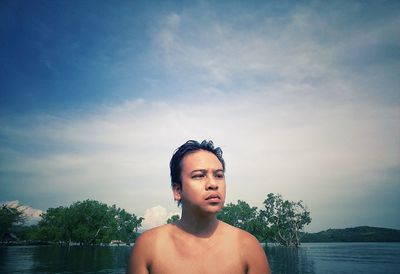 Portrait of shirtless young man standing against lake