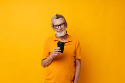 Young woman holding mobile phone against yellow background