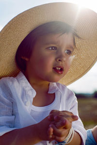 Baby boy in straw hat and blue pants sitting on a haystack in a field in autumn