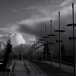 Man walking on footpath by street against sky